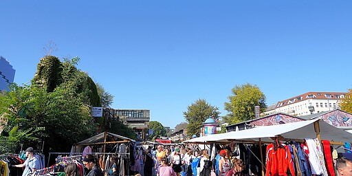 Flohmarktstände unter strahlend blauem Himmel Flohmarktstände reihen sich auf dem RAW-Gelände auf, während Besucher unter einem strahlend blauen Himmel stöbern.